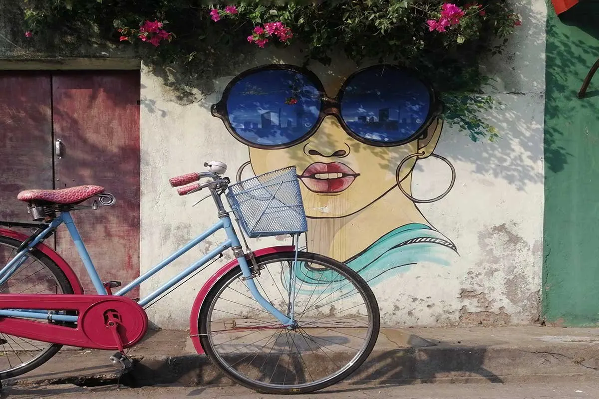 A vintage bicycle parked in front of a street-art mural of a woman in sunglasses