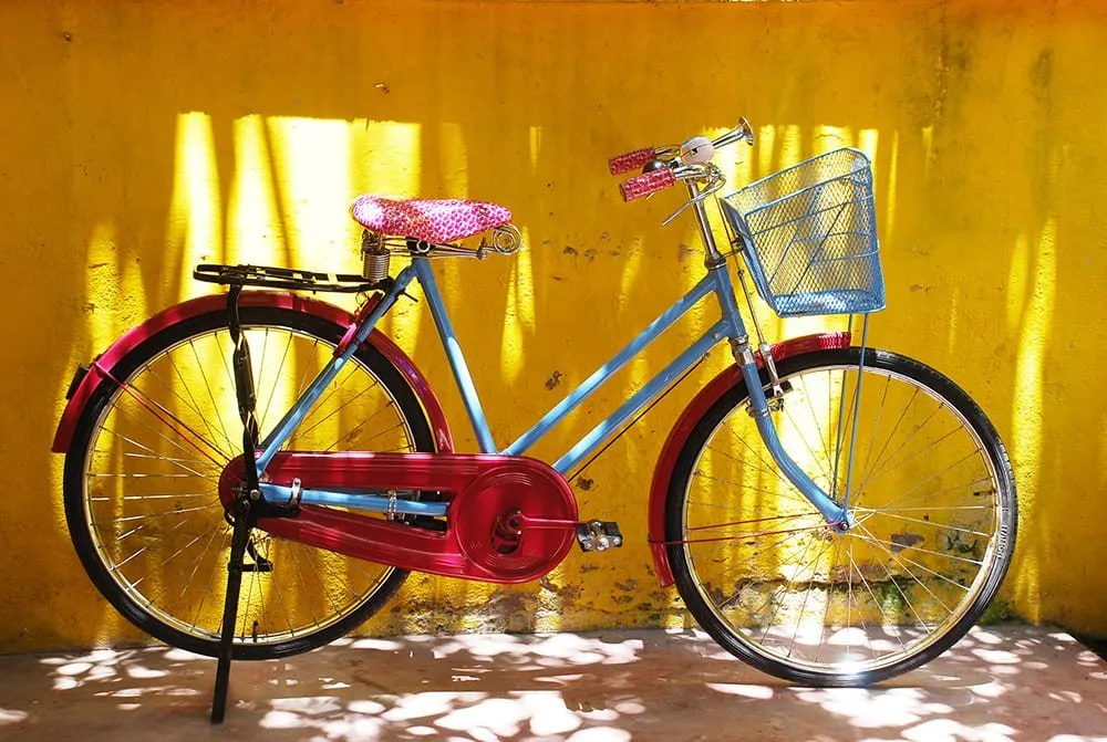 A blue and pink vintage bicycle against a golden yellow wall