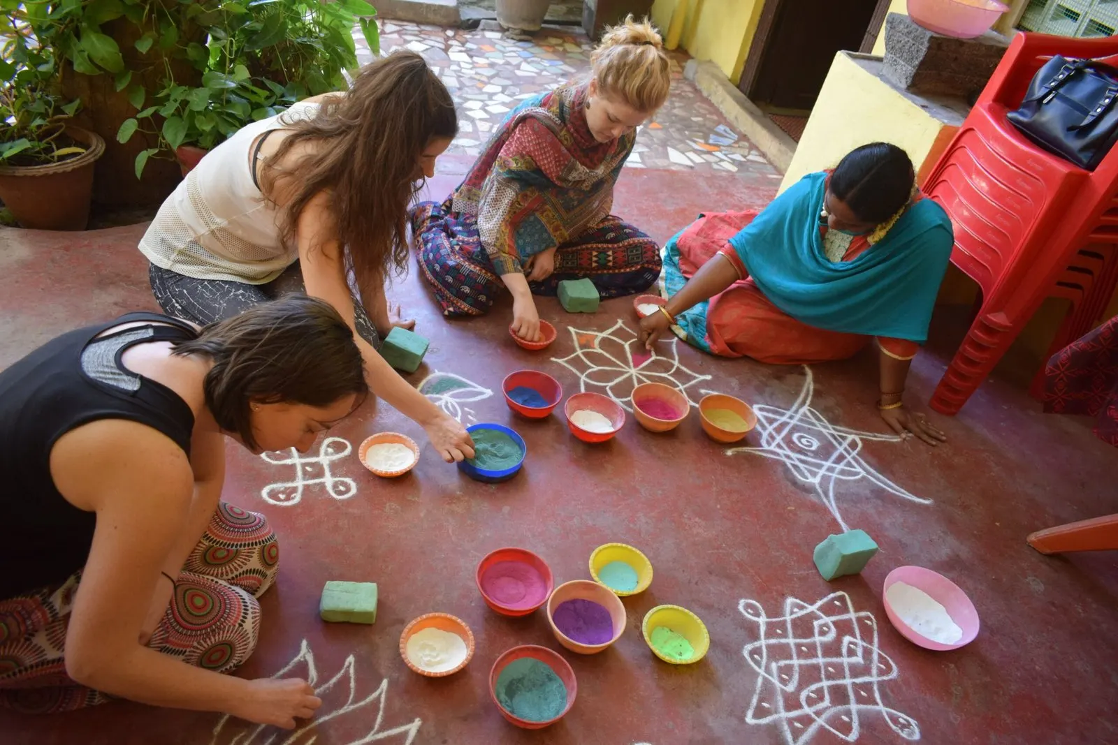 Guests and a teacher drawing kolam patterns with coloured powders