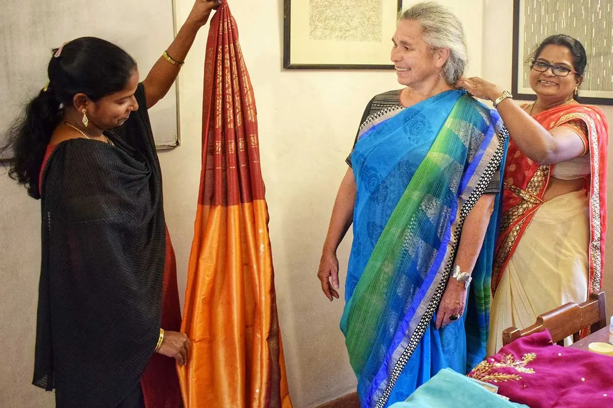 A teacher helps a guest drape a blue saree