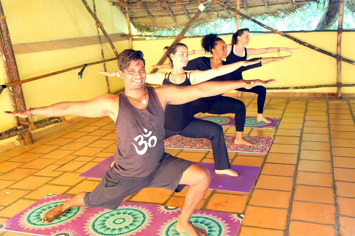 A yoga teacher leads a warrior pose in a sunny open-air studio